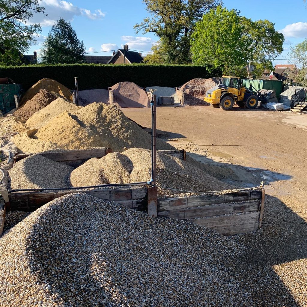 The aggregate yard with a yellow digger in the background, on the right, facing the right.