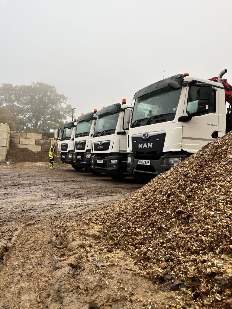 4 lorries, on the right are facing left, with a large pile of aggregate in the forefront.
